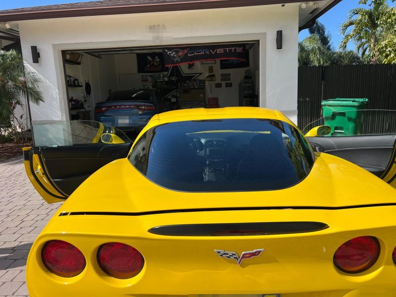 Yellow C6 Corvette from behind showing a tinted rear window, doors open in a driveway