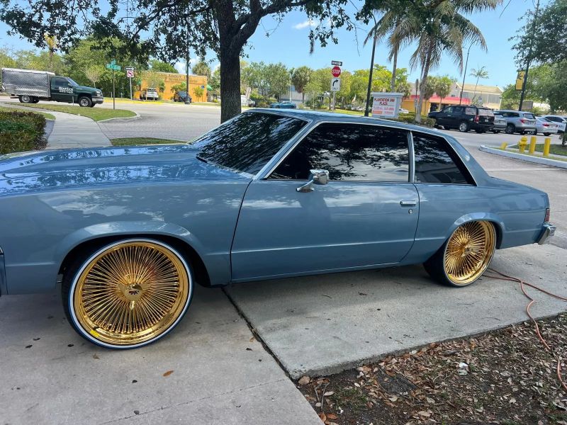 Light blue classic Chevrolet Malibu on gold wire wheels with dark tinted windows